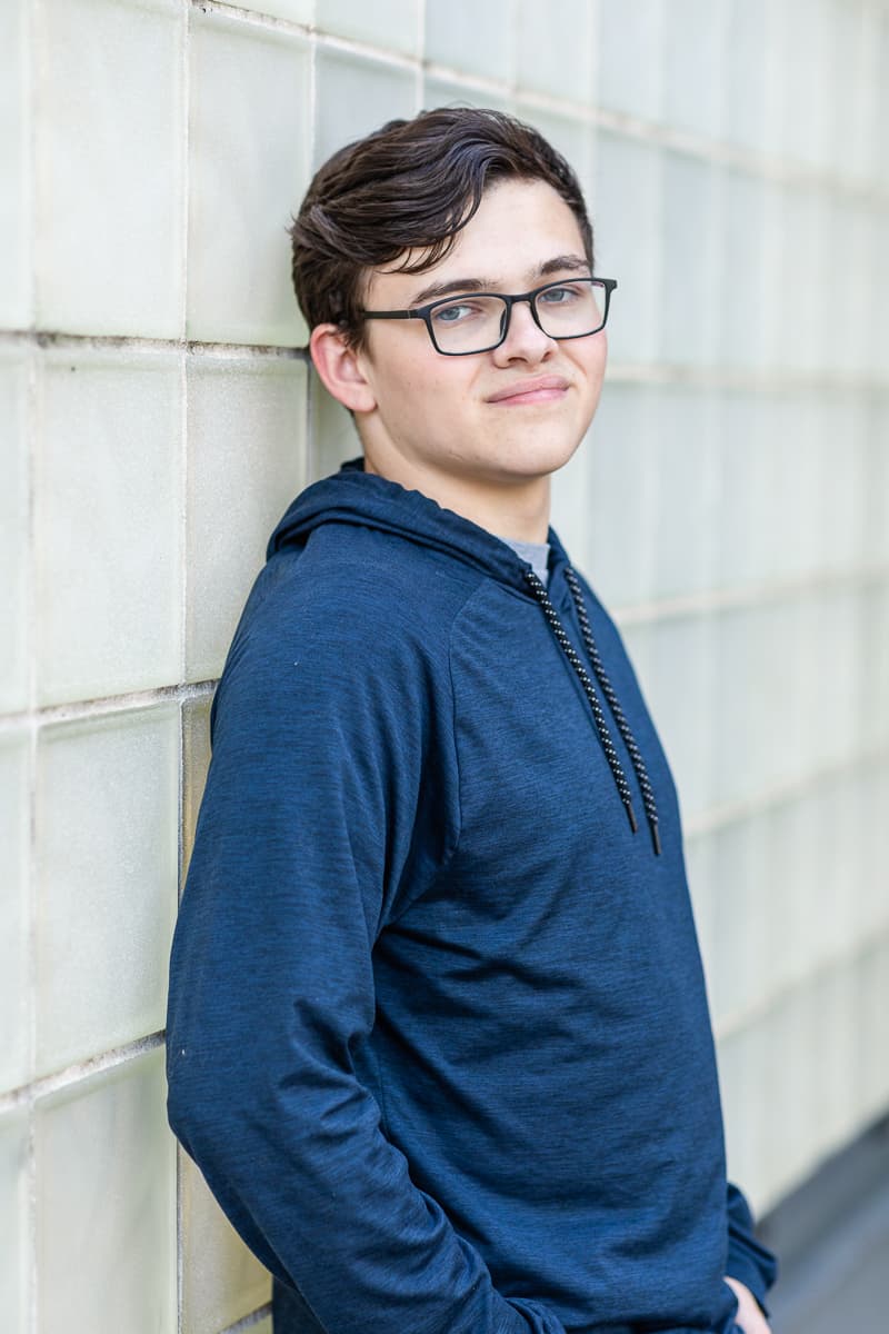 senior boy leans against glass block wall